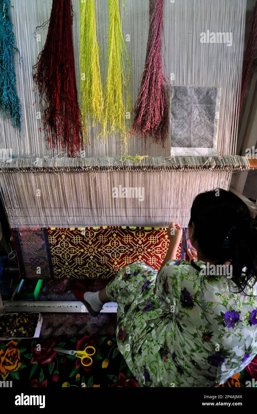 Les femmes ouzbèkes tissage d'un tapis traditionnel fait main dans un petit atelier de tapis dans la vieille ville de Boukhara, Ouzbékistan. Banque D'Images