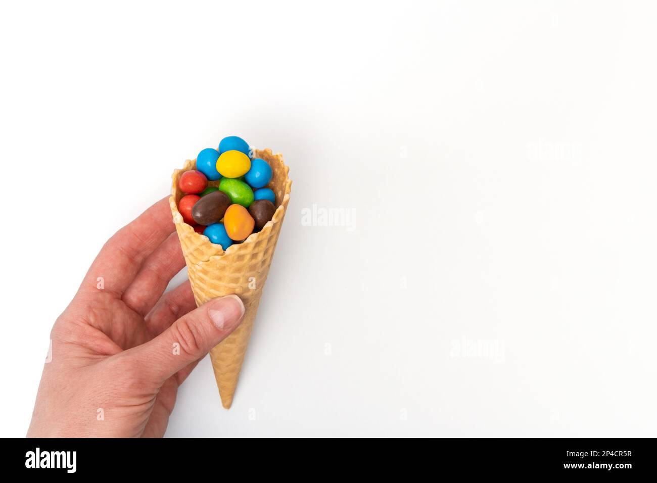 Une main tenant un cône de gaufre vide avec des bonbons ronds multicolores dispersés, des dragées. Des vacances amusantes. Bonbons pour enfants. Banque D'Images
