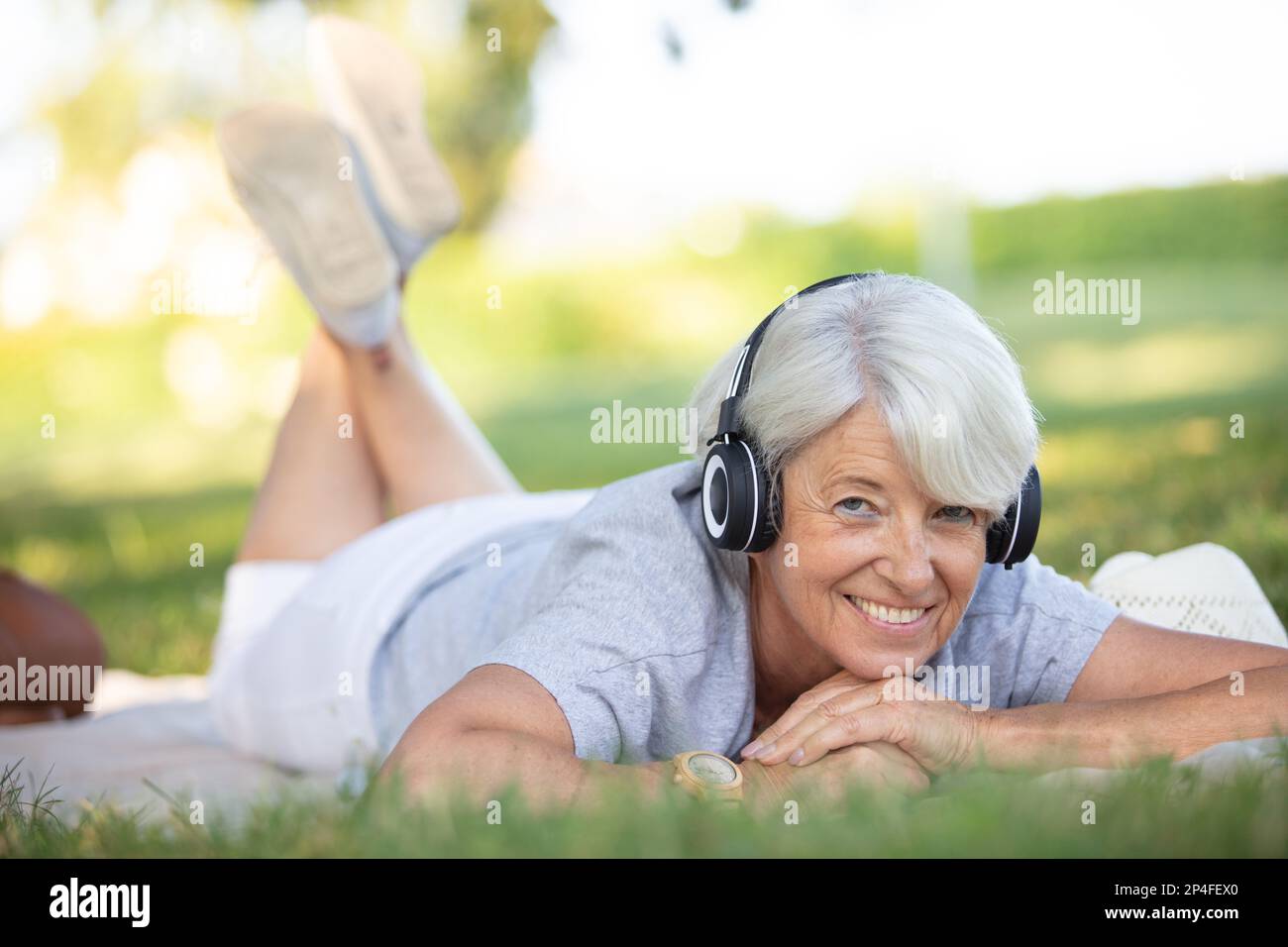 femme mûre écoutant de la musique tout en posant sur l'herbe Banque D'Images
