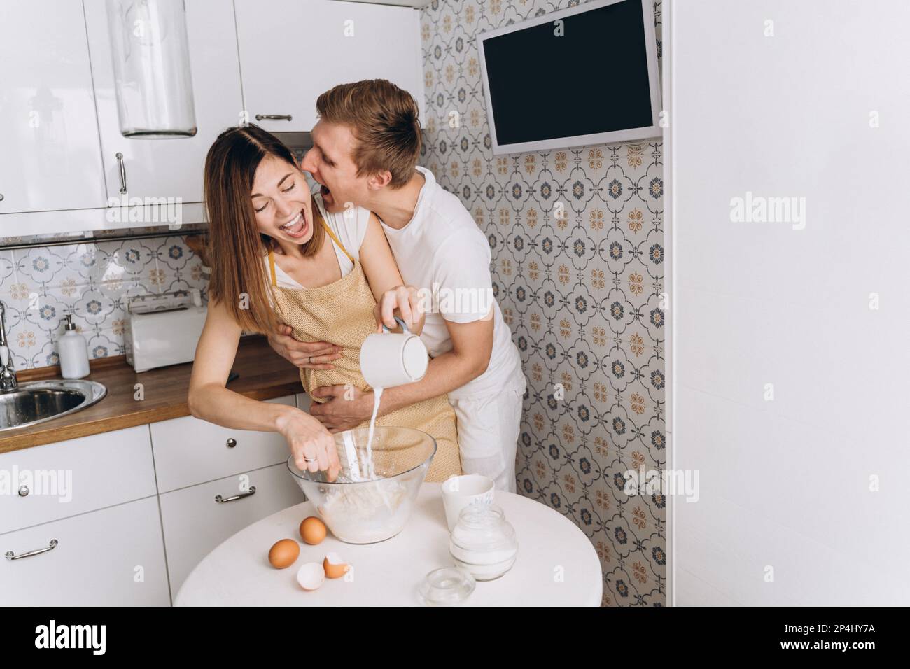 Un couple affectueux cuisine des crêpes dans la cuisine et des câlins Banque D'Images