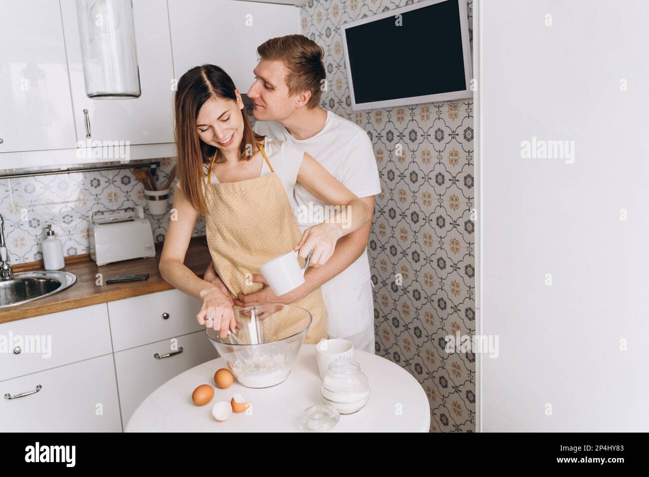 Un couple affectueux cuisine des crêpes dans la cuisine et des câlins Banque D'Images