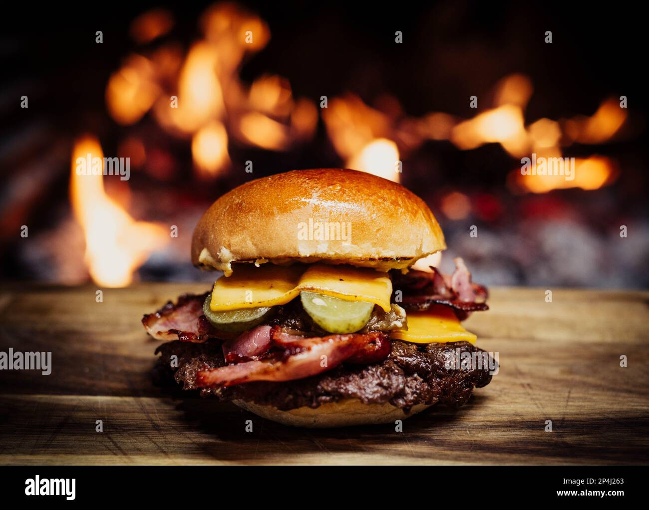 Cheeseburger écrasé sur une table en bois devant une cheminée. Banque D'Images