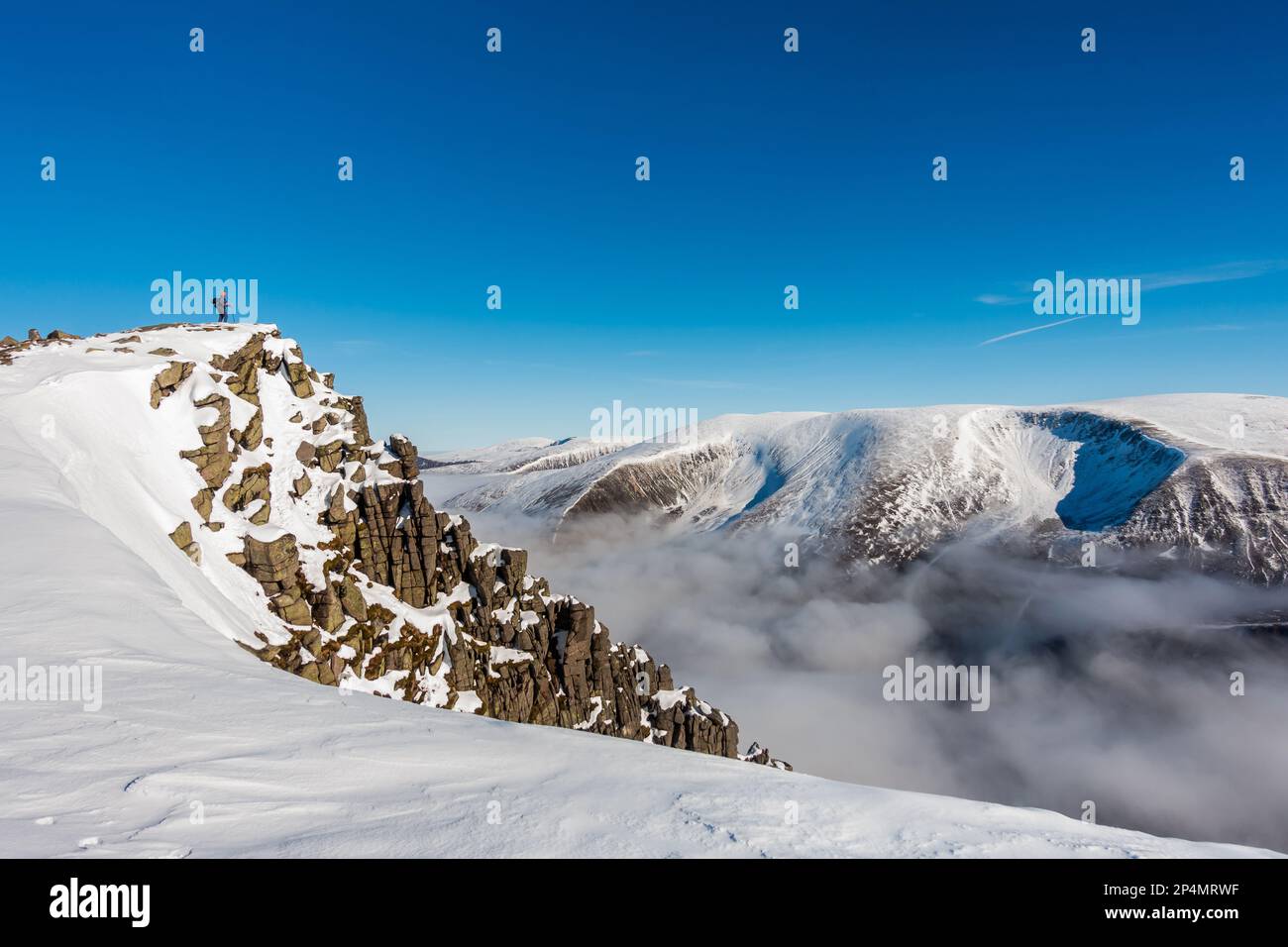 Un marcheur vu loin à gauche sur le sommet de la montagne Scottish Munro de Sgor Gaoith en hiver Banque D'Images