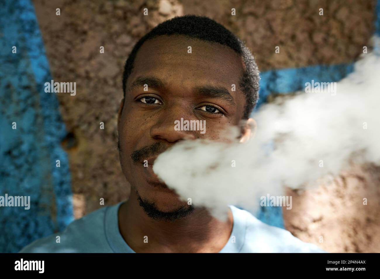 elfbar nachfüll pod läuft aus Visage du jeune homme afro-américain qui dégage un nuage de vapeur blanche  épaisse de sa bouche tout en fume la cigarette électronique et en regardant  la caméra Photo Stock