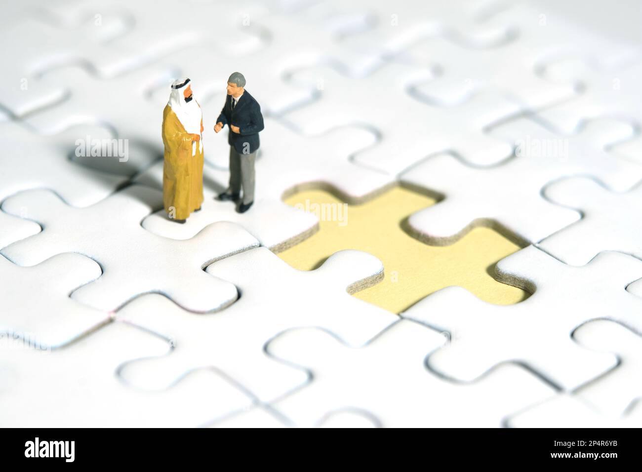 Photographie miniature de personnage de jouet de personnes. Concept de partenariat. Un Sultan et un homme d'affaires font un accord de poignée de main au-dessus du puzzle avec la tarte manquante Banque D'Images