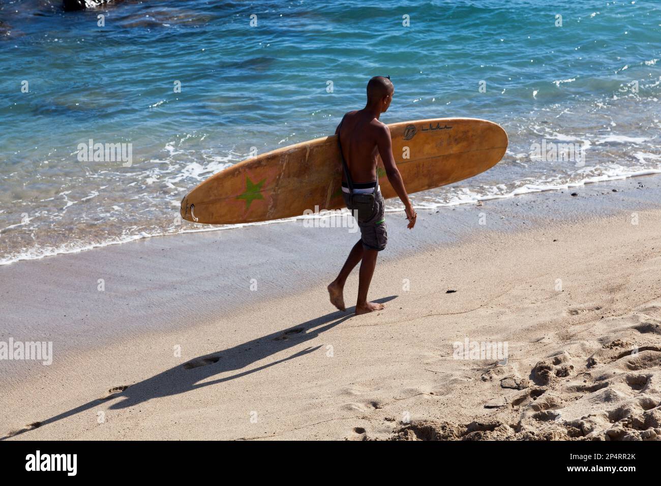 Saint Gilles les bains, la Réunion - 13 juin 2017 : adolescent tenant sa planche de surf tout en marchant au bord de la Plage des roches noires (plage de t Banque D'Images