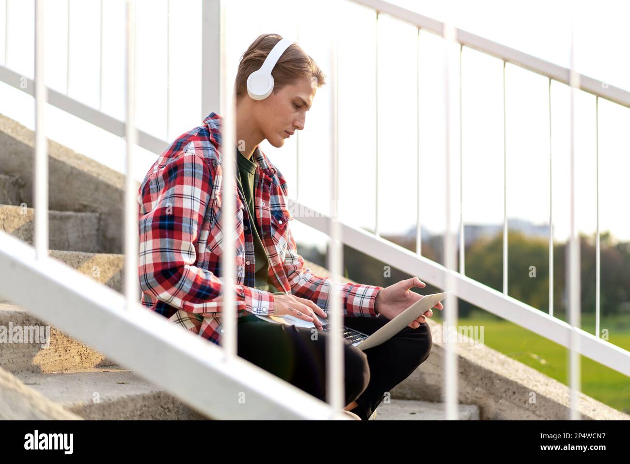 Femme étudiante dans un casque assis sur les marches de la ville et utilisant son ordinateur portable. Banque D'Images