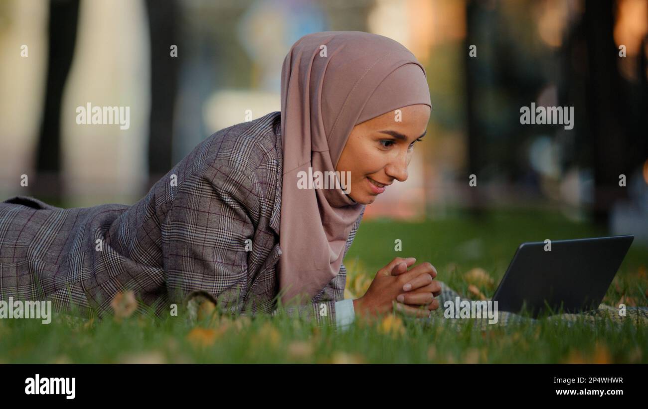 Ethnique musulmane femme d'affaires islamique fille dans hijab femme employeur couché herbe pelouse dans le parc à l'extérieur femme enseignant en ligne mentor faire appel vidéo chat Banque D'Images