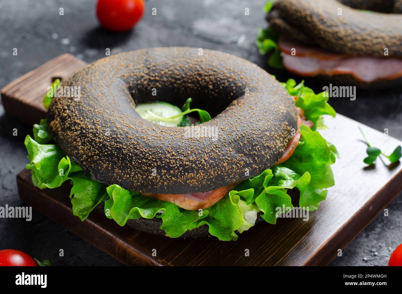 Sandwiches bagels noirs avec concombres, salade et jambon sur bois et fond sombre, délicieux en-cas ou petit déjeuner Banque D'Images