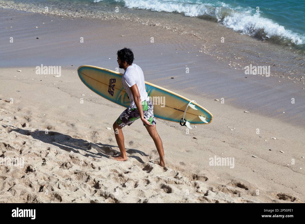 Saint-Gilles les bains, la Réunion - 13 juin 2017 : jeune homme tenant sa planche de surf tout en marchant au bord de la Plage des roches noires (plage de Banque D'Images