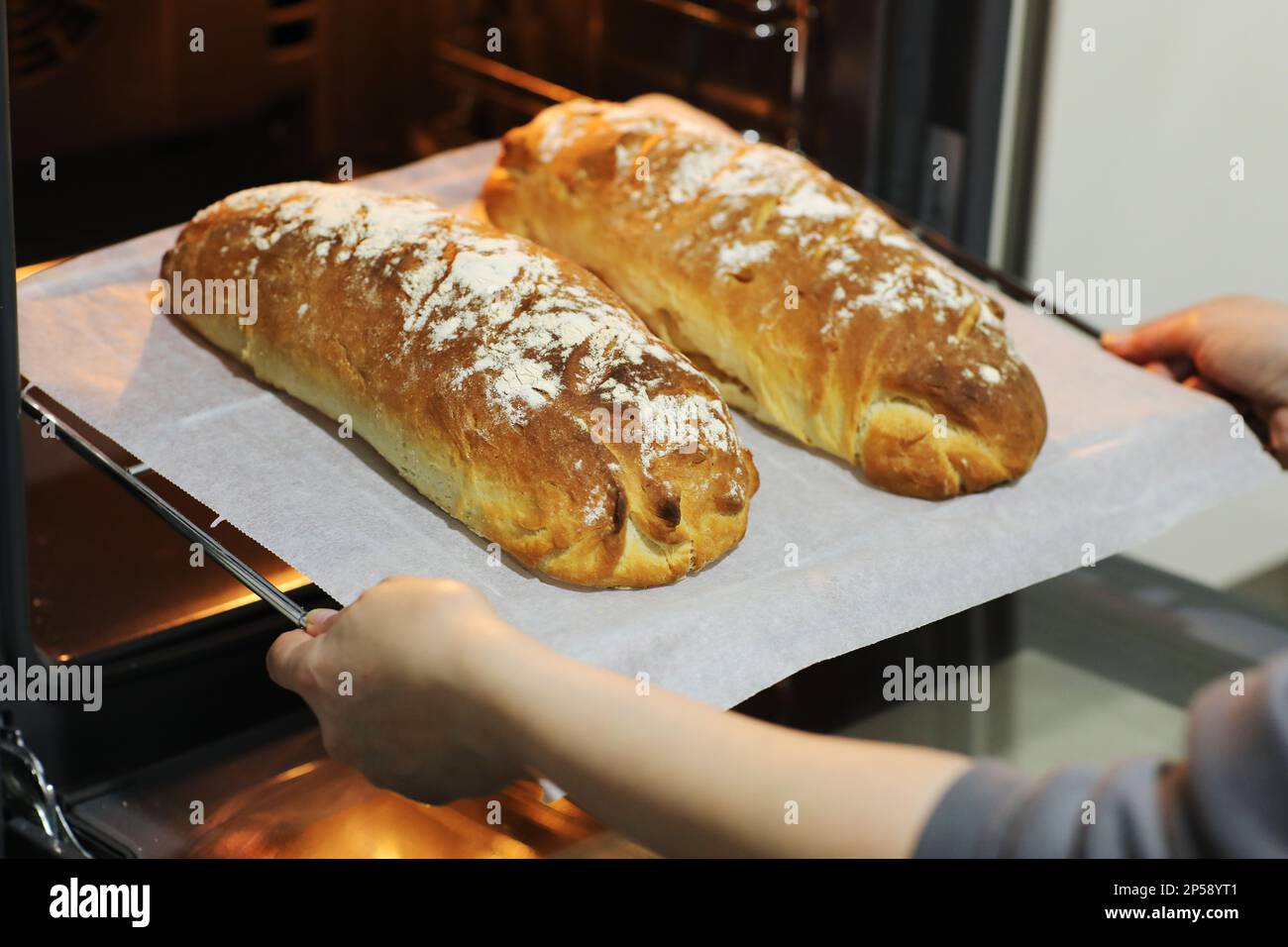 Photo de femmes les mains de prendre des pains chauds frais cuits d'un four électrique sur un plateau métallique dans la cuisine à la maison. Pain rustique fait maison, baki Banque D'Images