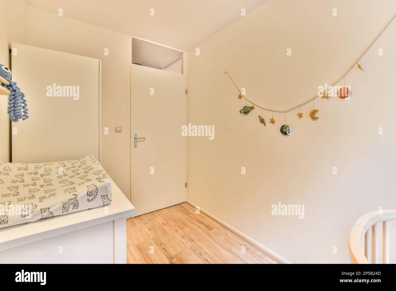 une chambre pour enfants avec des murs blancs et du parquet sur le mur, il y a un animal bourré suspendu au-dessus du lit Banque D'Images