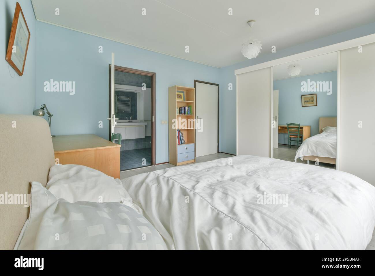 un lit dans une chambre avec des murs bleus et des draps blancs sur le cheveu est au-dessus de la tête de lit Banque D'Images
