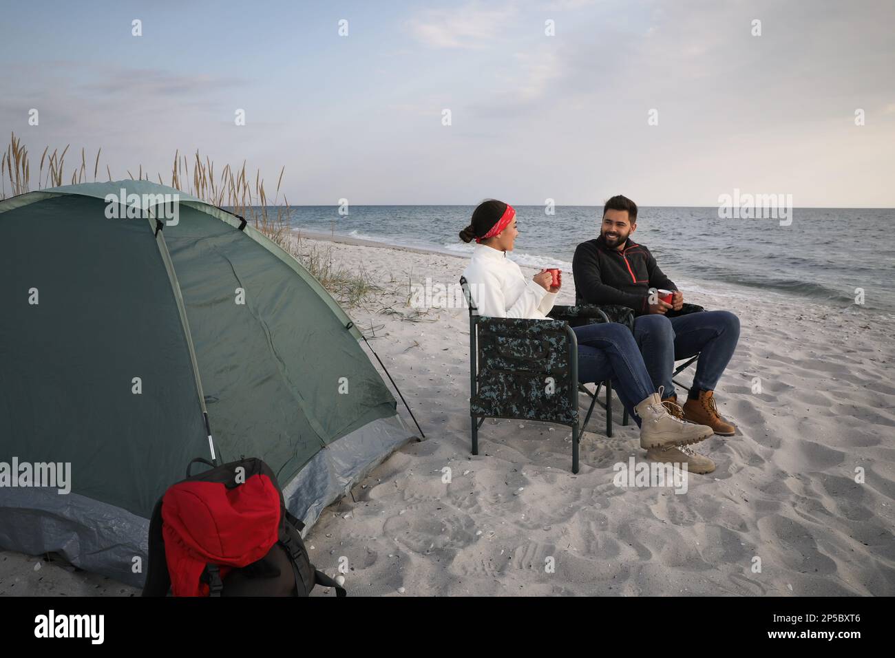 Couple avec boissons chaudes près de tente de camping sur la plage Banque D'Images