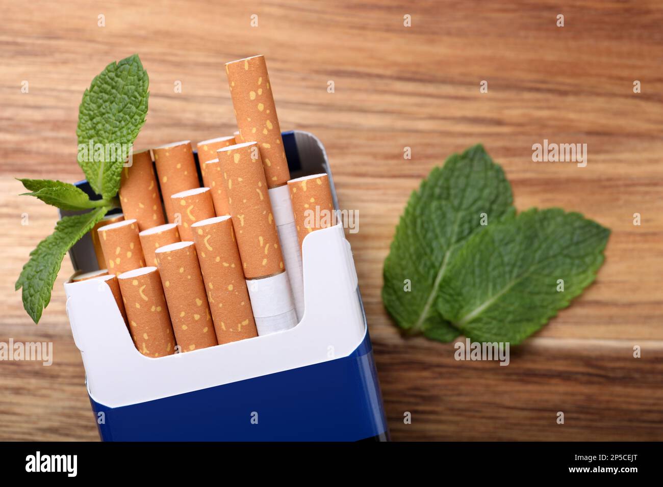 Paquet de cigarettes de menthol et feuilles de menthe sur table en bois, plat Banque D'Images