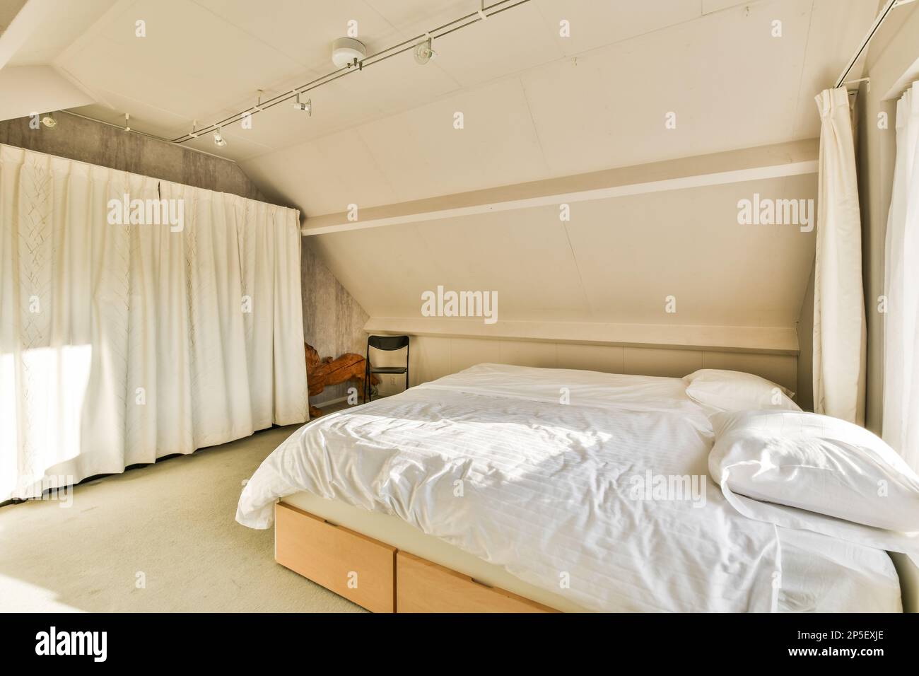 un lit dans une chambre avec des draps blancs et des rideaux suspendus du plafond au mur derrière eux Banque D'Images