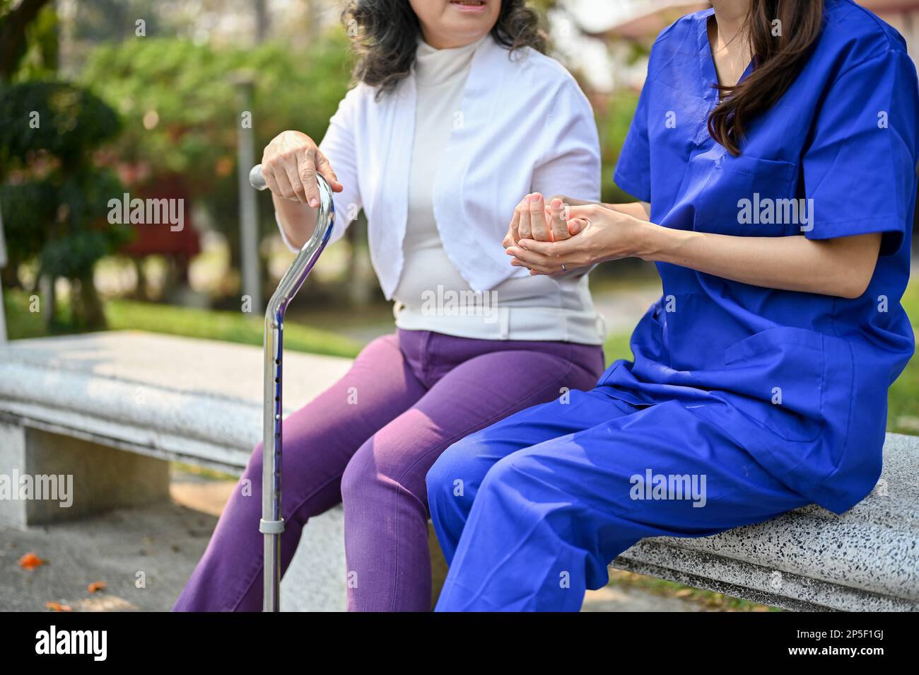 Image rognée d'une infirmière asiatique soignante ou d'un soignant tenant la main d'une vieille patiente, parlant et soutenant tout en se relaxant dans le parc Banque D'Images