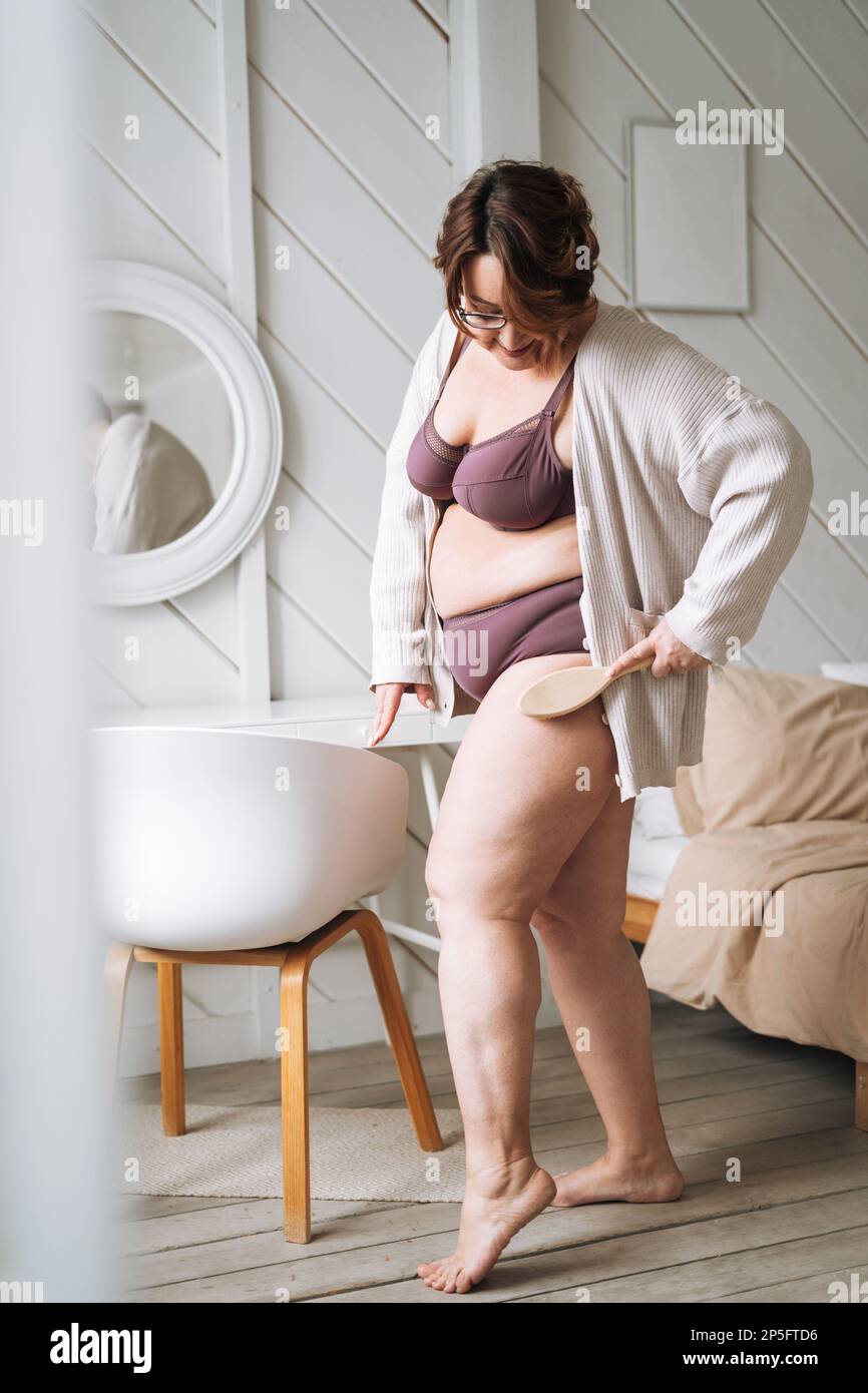 Moyenne âge plus taille femme en sous-vêtements faisant un massage corporel avec brosse en bois sèche dans la salle de bains à la maison Banque D'Images