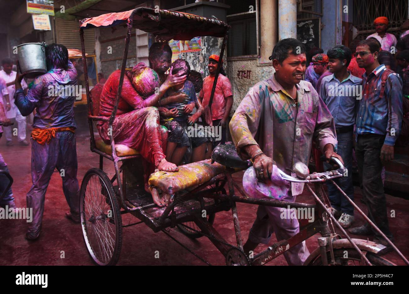 A woman, drenched in colored water, cover s the face of a child as they ride a rickshaw past people celebrating Holi festival outside Banke Bihari temple in Vrindavan, India, Wednesday, March 27, 2013. Holi, the Hindu festival of colors that also marks the advent of spring, is being celebrated across the country Wednesday. (AP Photo/Altaf Qadri) Banque D'Images