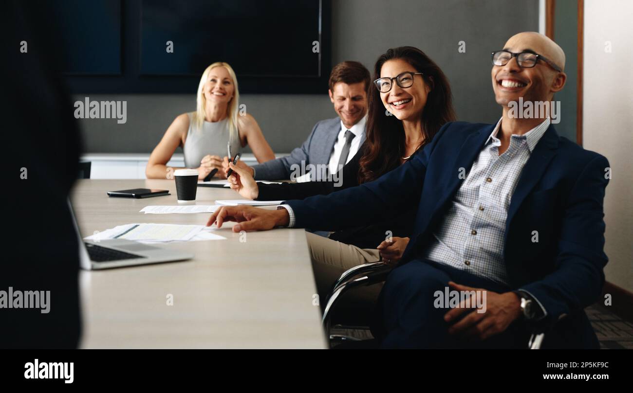 Groupe de gens d'affaires divers assis dans une salle de réunion, souriant et faisant attention pendant qu'ils entendent une présentation. Professionnels ayant un m Banque D'Images