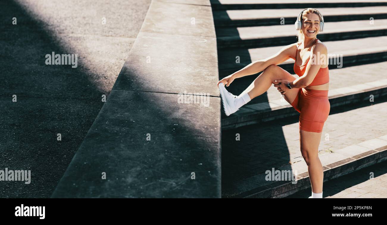 Bonne femme de sport qui fait une pause pour courir à l'extérieur. FIT femme portant un casque sans fil et des vêtements de sport. Femme sportive effectuant un entraînement cardio. Banque D'Images