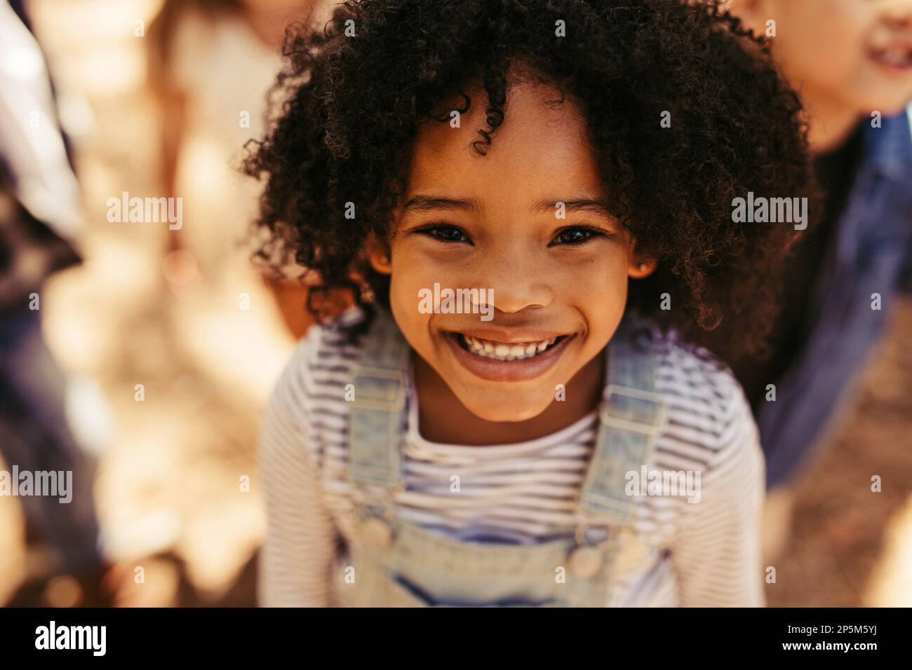 Close up portrait of smiling african girl avec des amis à l'arrière-plan. Petite fille à la caméra à l'extérieur. Banque D'Images