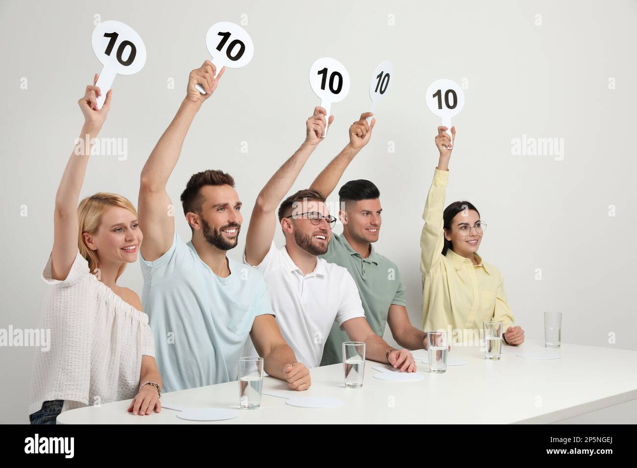 Panel de juges portant des affiches avec le score le plus élevé à la table sur fond blanc Banque D'Images