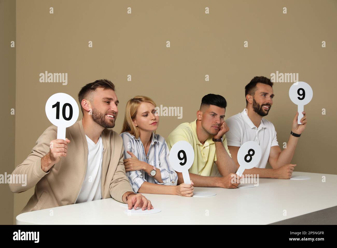 Panel de juges présentant différents signes de score à la table sur fond beige Banque D'Images