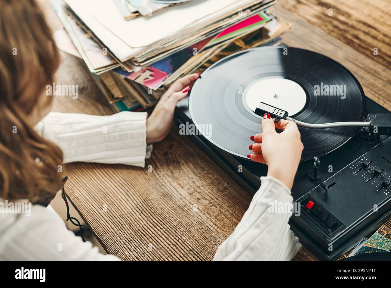 Jeune femme écoutant de la musique à partir d'un lecteur de disques en vinyle. Lecture de musique sur le lecteur de platine. Une femme qui profite de la musique d'une ancienne collection de disques à la maison. Banque D'Images