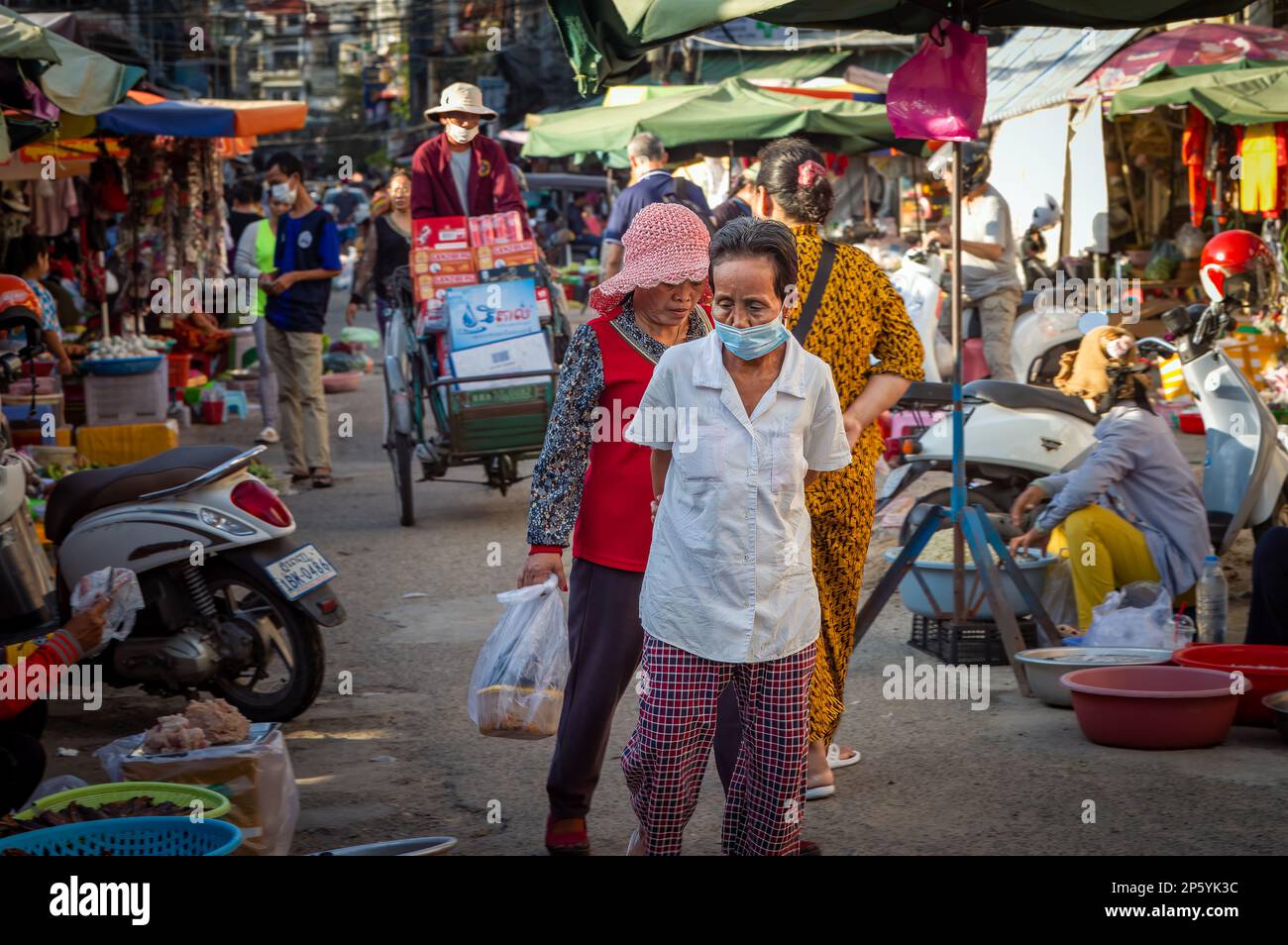 Les clients parcourent un marché de rue à Phnom Penh tandis qu'un chauffeur de cyclo passe dans des étuis pour le transport de bière et de boissons. Banque D'Images