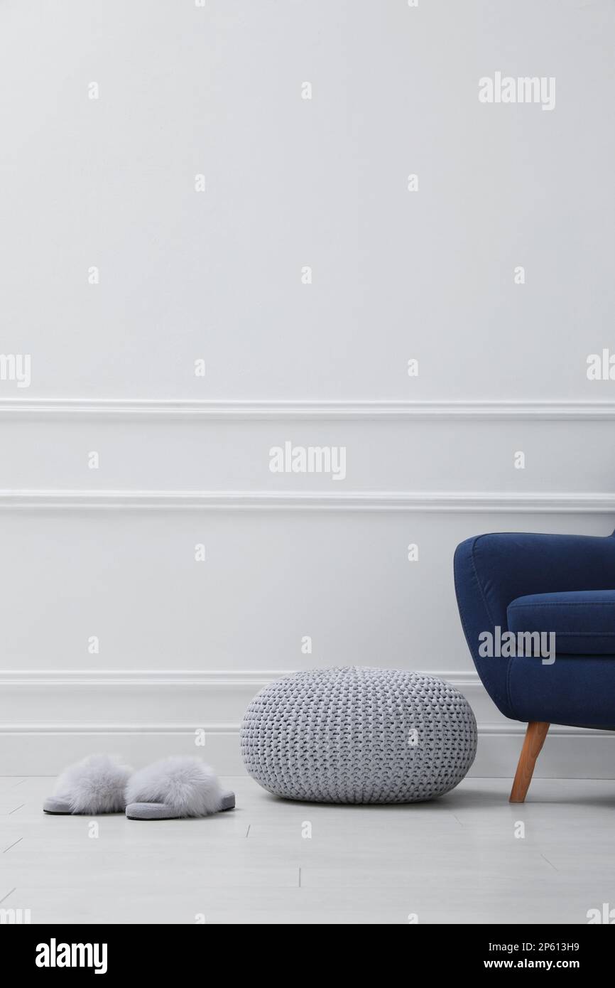 Pouf tricoté, pantoufles et fauteuil près du mur blanc à l'intérieur. Espace pour le texte Banque D'Images