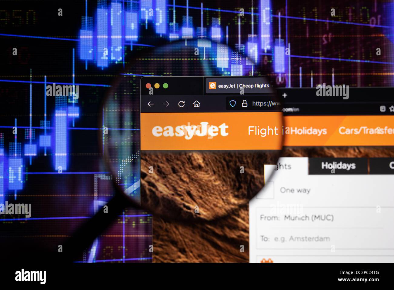 Logo de la compagnie aérienne Easy Jet sur un site Web avec des développements flous du marché boursier en arrière-plan, vu sur un écran à travers une loupe Banque D'Images