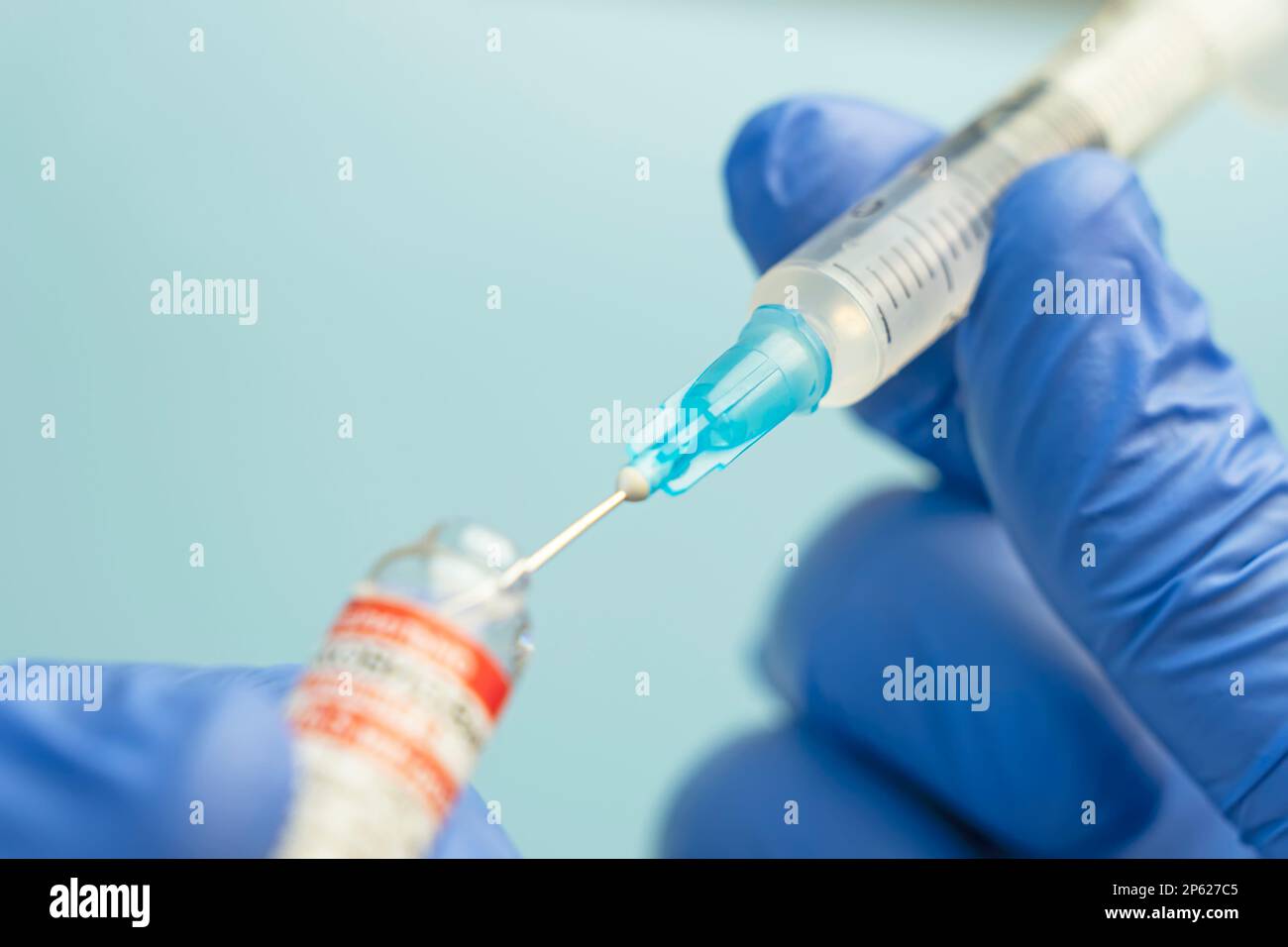 Macro d'une seringue hypodermique ou d'une aiguille remplie d'un vaccin d'ARNm provenant d'un flacon sur fond bleu Banque D'Images