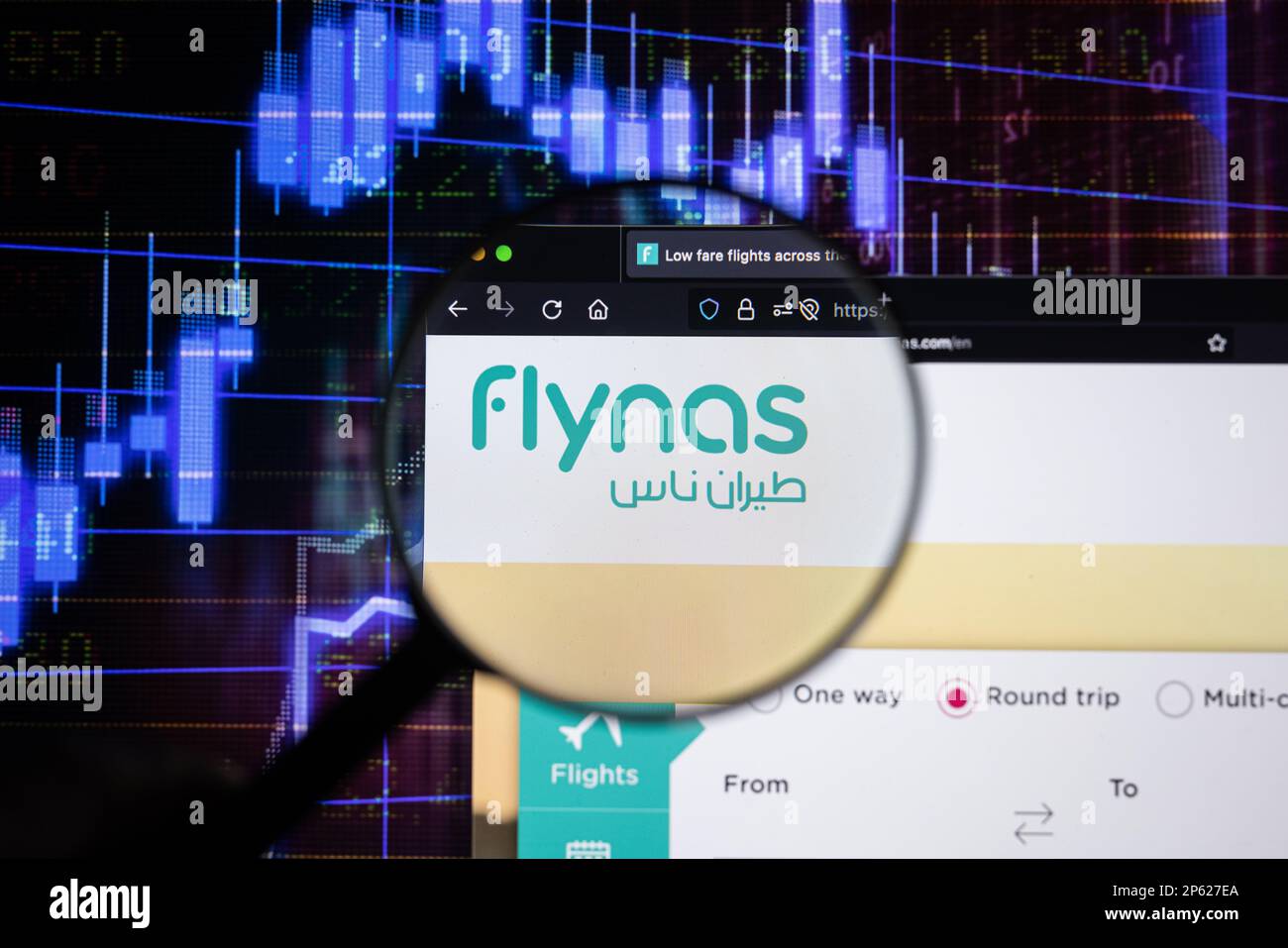 Le logo de la compagnie aérienne Flynas sur un site Web avec des développements flous de marché boursier en arrière-plan, vu sur un écran d'ordinateur à travers une loupe Banque D'Images