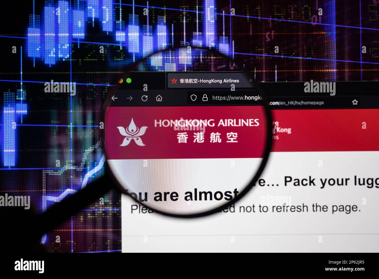 Logo de la compagnie Hongkong Airlines sur un site Web avec des développements flous de marché boursier en arrière-plan, vu sur un écran à travers une loupe Banque D'Images