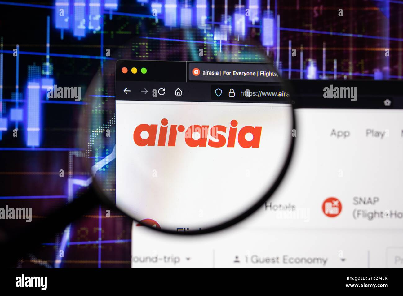 Logo de la compagnie aérienne AirAsia sur un site Web présentant des développements flous du marché boursier en arrière-plan, vu sur un écran à travers une loupe Banque D'Images