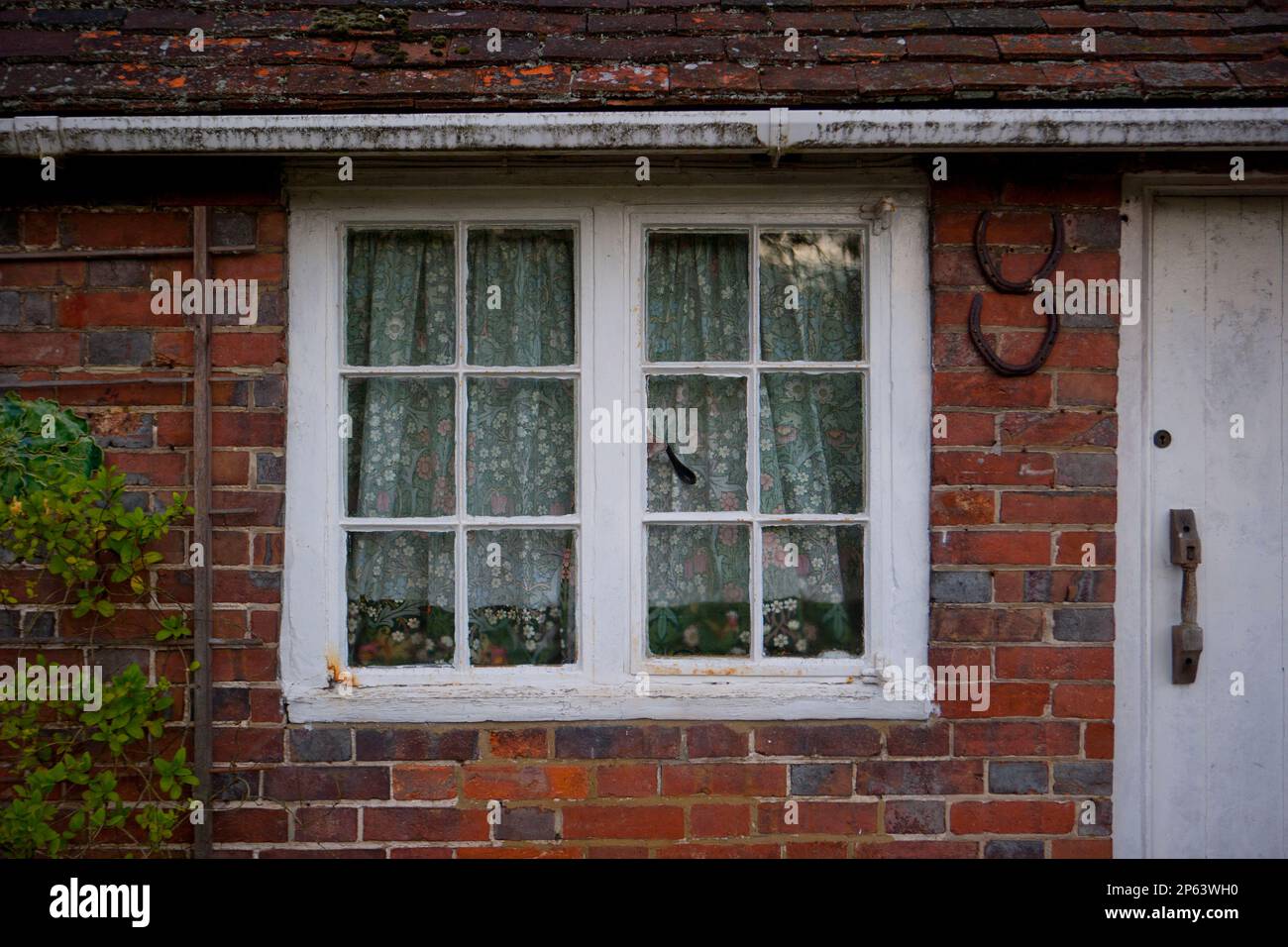 Ancienne maison de campagne en briques blanches fenêtres avec rideaux fleuris Banque D'Images