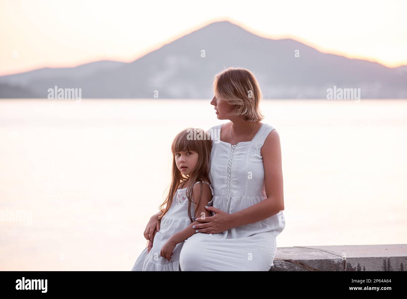 Mère enceinte du millénaire assis avec sa fille au coucher du soleil au bord de la mer. Une femme d'âge moyen épouse une petite fille. Le voyage d'un seul parent. Grossesse en santé Banque D'Images