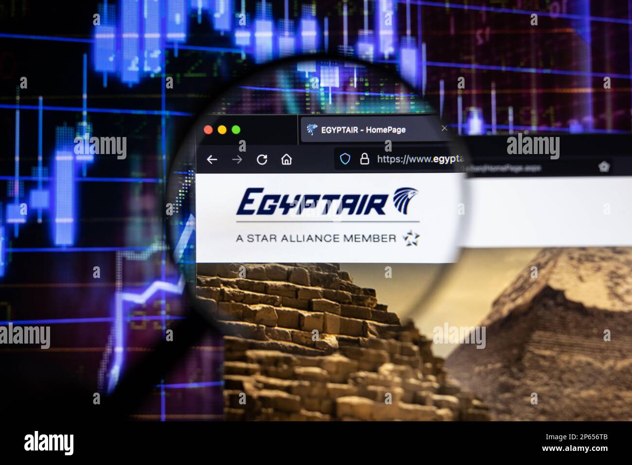 EgyptAir compagnie aérienne logo sur un site Web avec des développements flous de marché boursier en arrière-plan, vu sur un écran à travers une loupe Banque D'Images