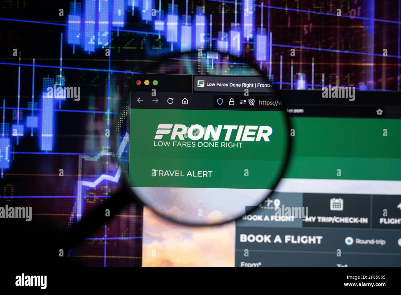 Logo de la compagnie aérienne Frontier sur un site Web avec des développements flous du marché boursier en arrière-plan, vu sur un écran à travers une loupe Banque D'Images