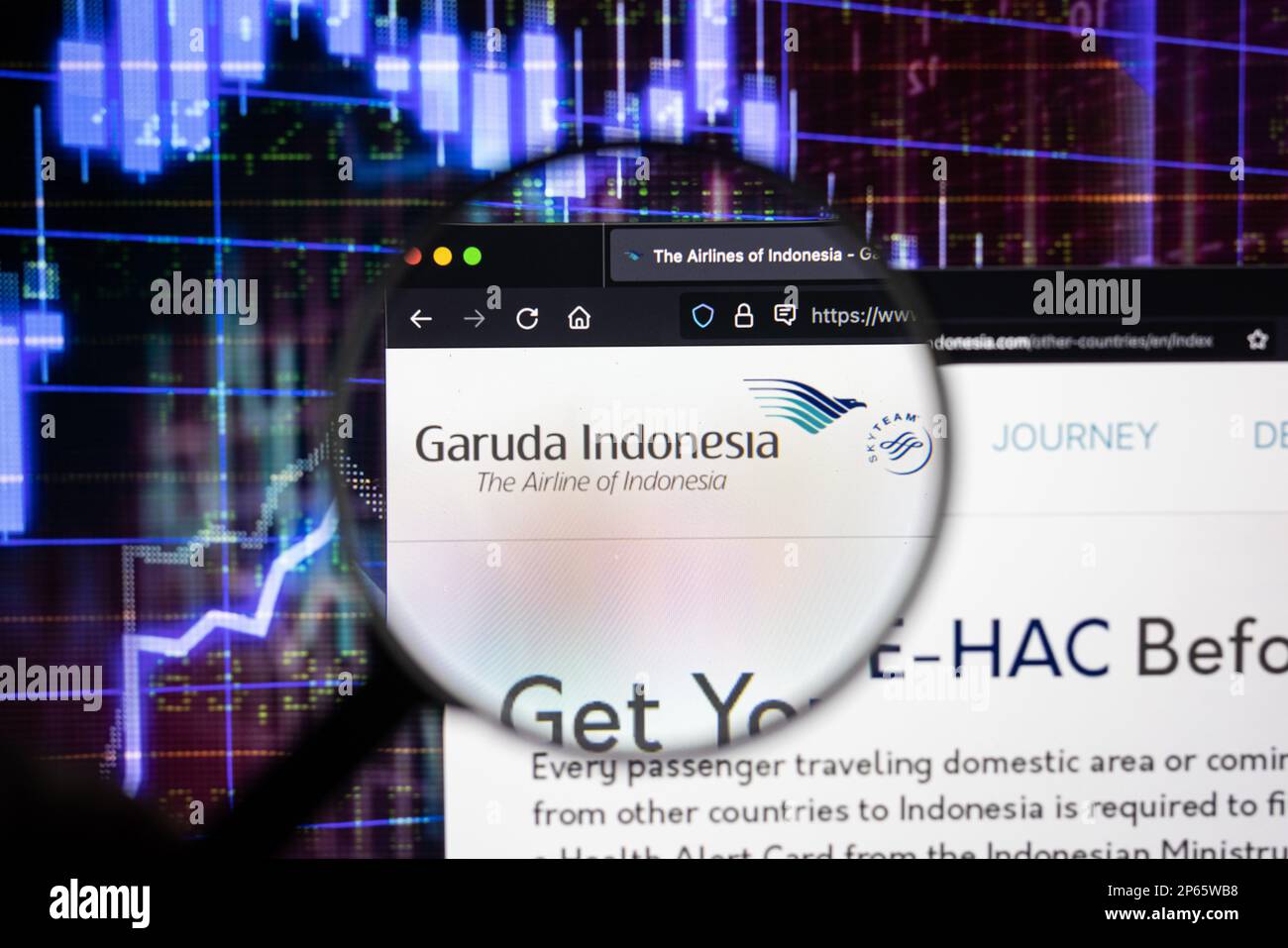 Logo de la compagnie aérienne Garuda Indonesia sur un site web avec des développements flous du marché boursier en arrière-plan, sur un écran à travers une loupe Banque D'Images