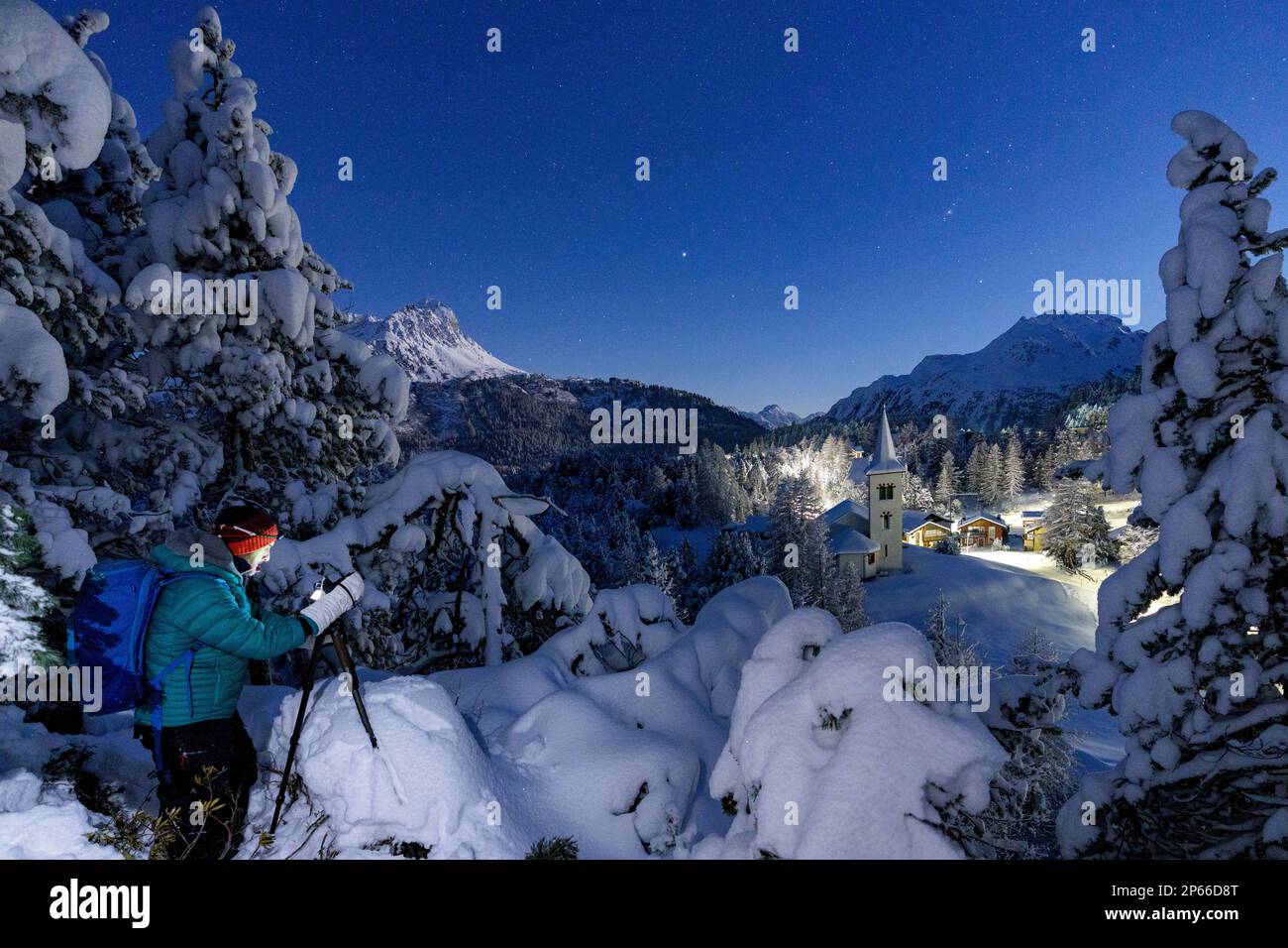 Un homme photographiant l'ancienne Chiesa Bianca de nuit debout dans une forêt enneigée, Maloja, Engadine, canton de Graubunden, Suisse, Europe Banque D'Images