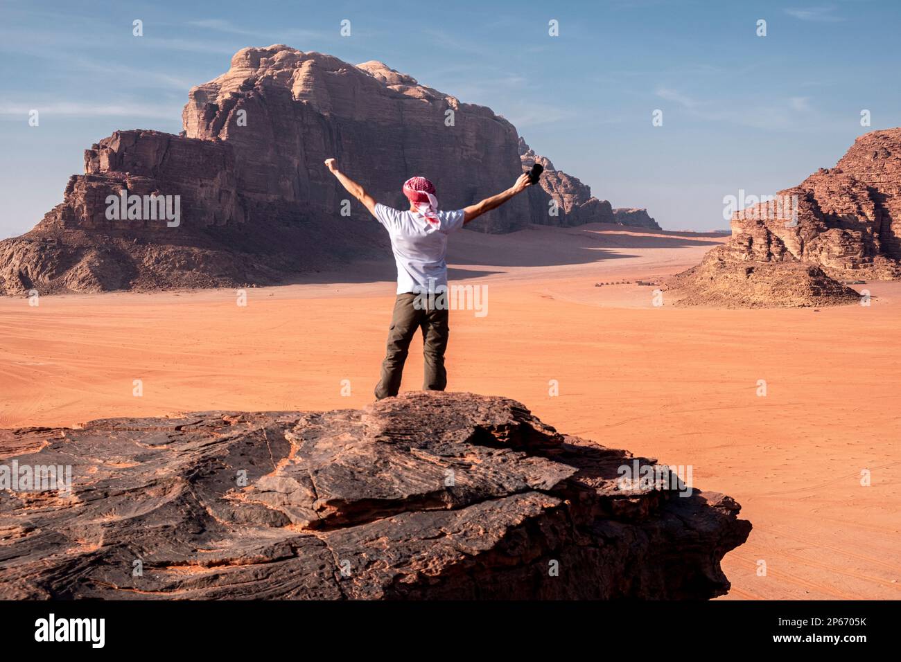 Un homme avec un turban et ses mains soulevées debout sur un rocher dans le désert de Wadi Rum, site du patrimoine mondial de l'UNESCO, Jordanie, Moyen-Orient Banque D'Images