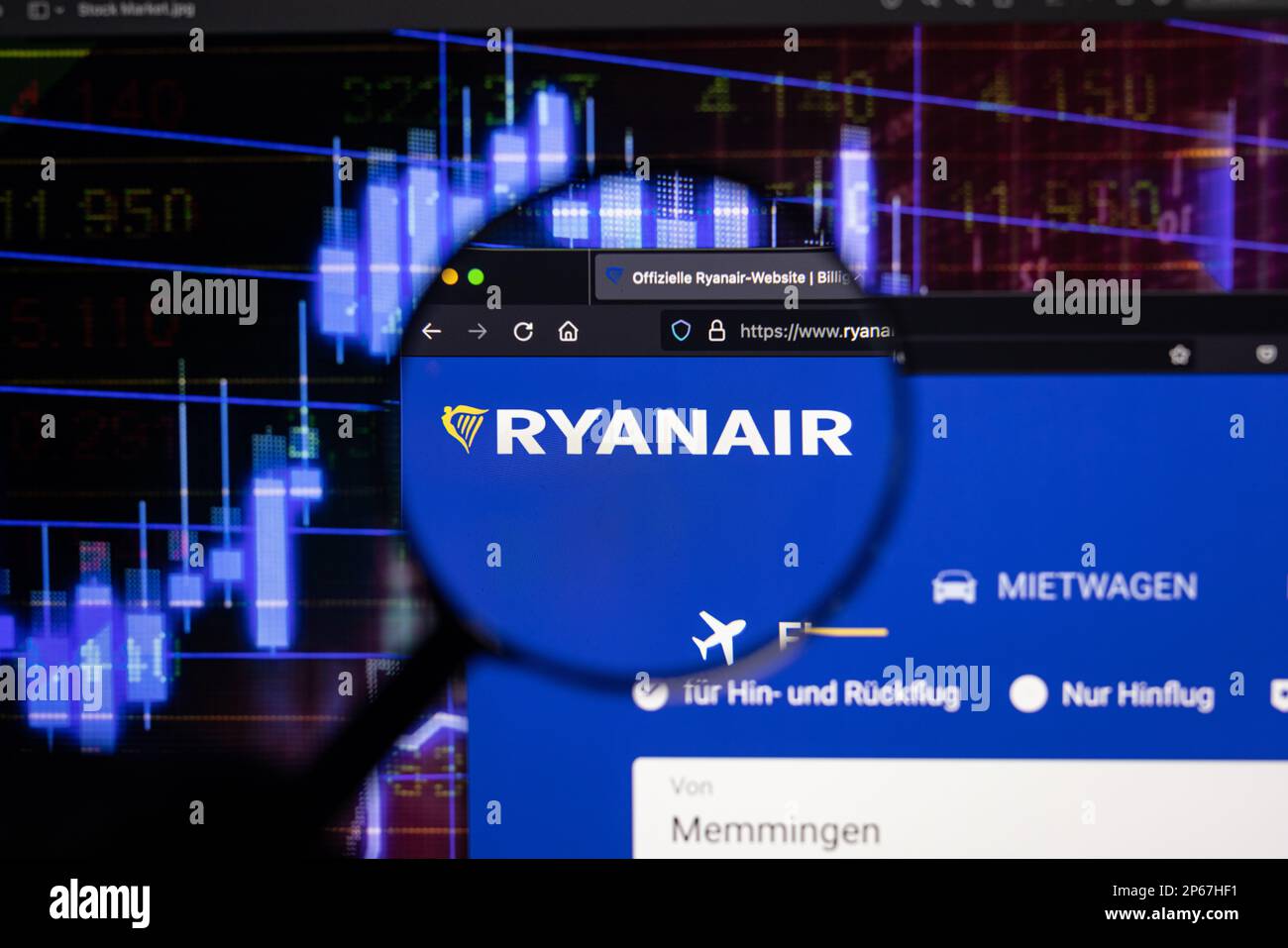 Logo de la société Ryanair sur un site web avec des développements flous de marché boursier en arrière-plan, vu sur un écran d'ordinateur à travers une loupe Banque D'Images
