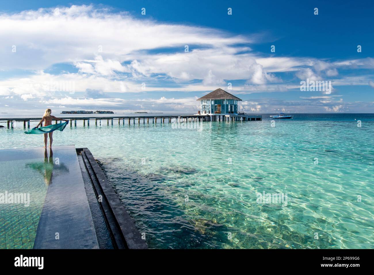 Jeune femme marchant le long du bord d'une piscine à débordement, Maldives Banque D'Images