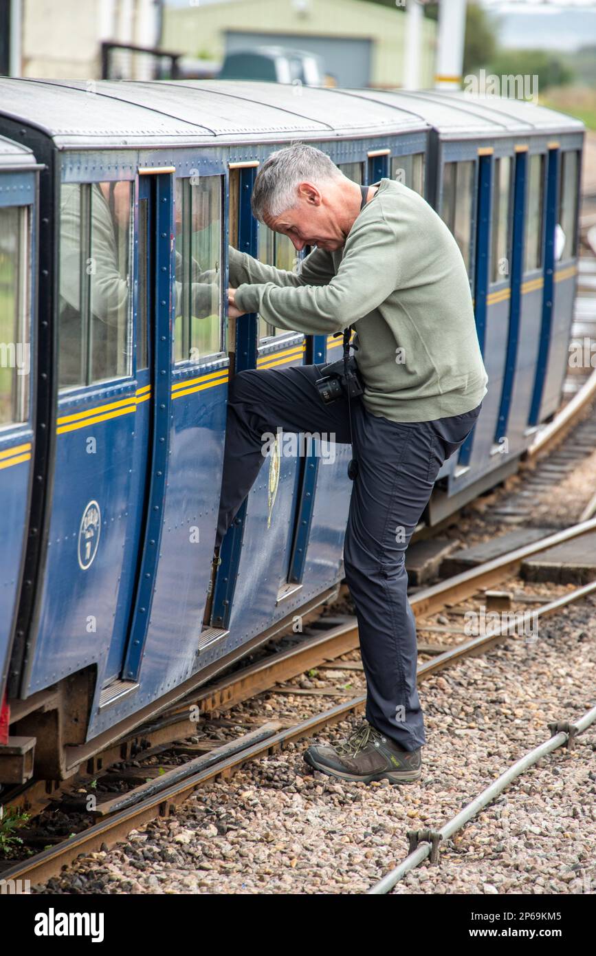 Un homme âgé monte à bord d'une petite voiture à la gare de New Romney pour une promenade sur le train à vapeur miniature Romney, Hythe & Dymchurch (RH&DR) Banque D'Images