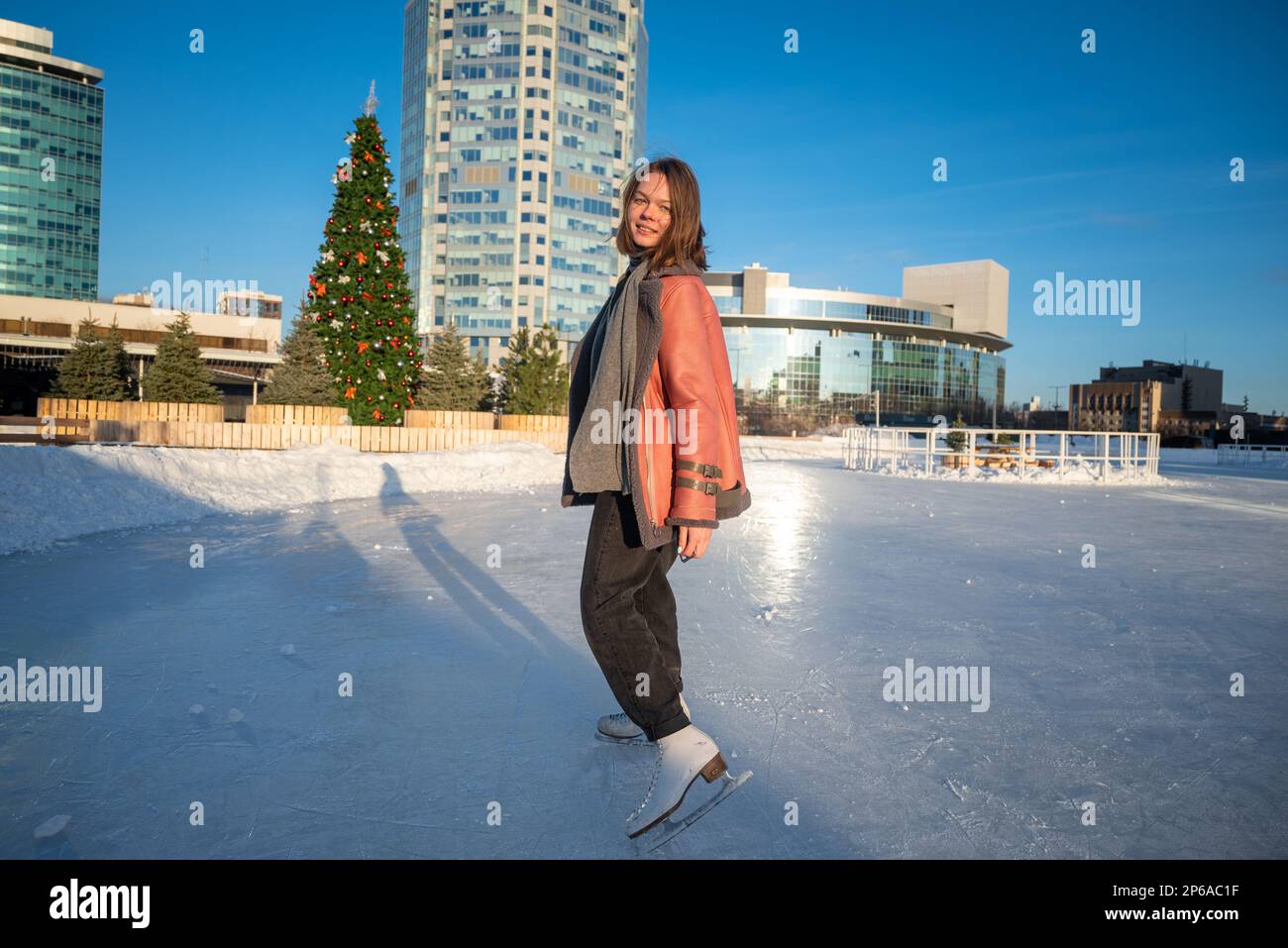 une jeune belle fille sur skate dans un manteau de peau de mouton sur une  patinoire avec la toile de fond de la métropole et les rayons du soleil  Photo Stock -