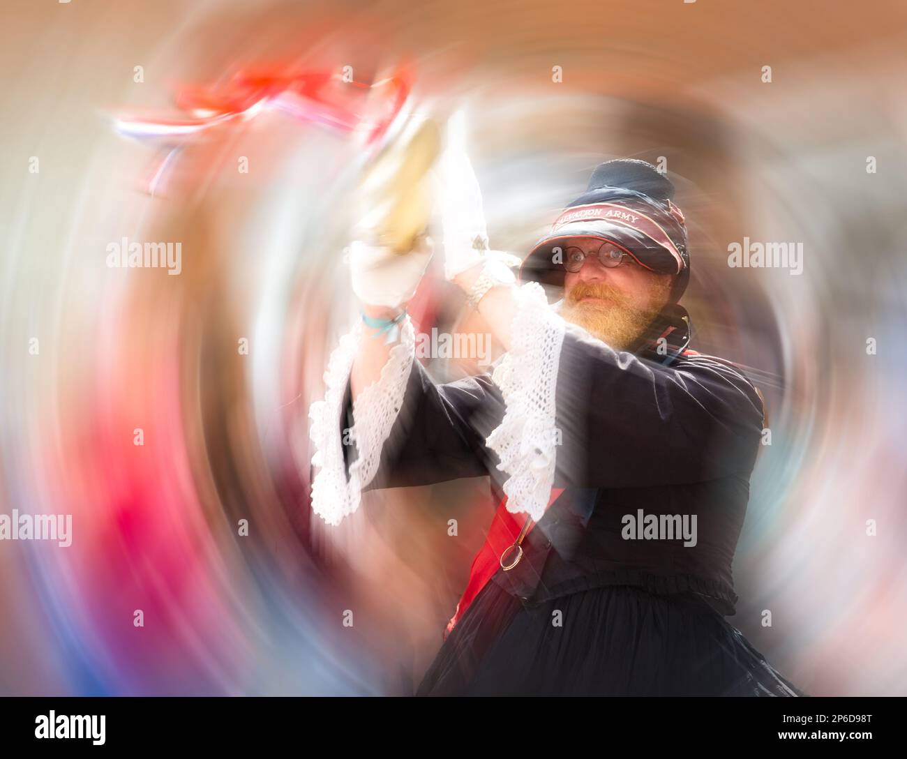 Un homme avec une barbe portant un uniforme féminin de l'Armée du Salut dansant et faisant des cercles avec le tambourin qu'il joue Banque D'Images