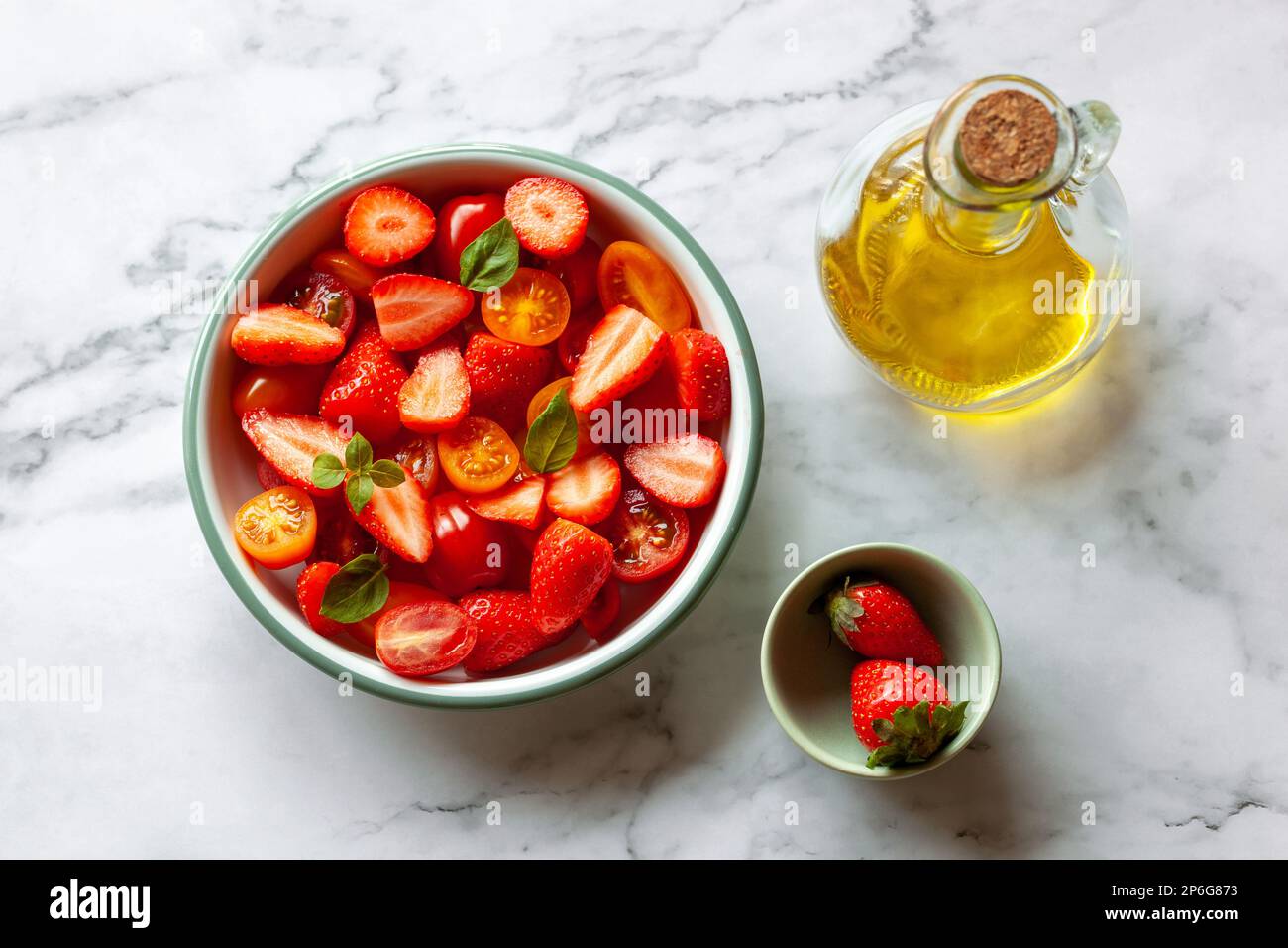 portion de salade de cerises aux fraises et aux tomates décorée de feuilles de basilic, fond en marbre, vue sur le dessus Banque D'Images