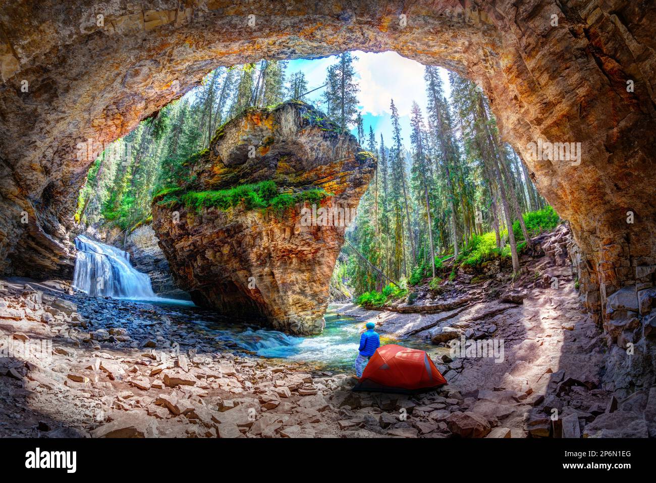 Le randonneur se tient à l'extérieur de sa tente de camping à Hidden Cave avec chute d'eau et roche calcaire dans le canyon Johnston, dans le parc national Banff, dans l'RO canadien Banque D'Images